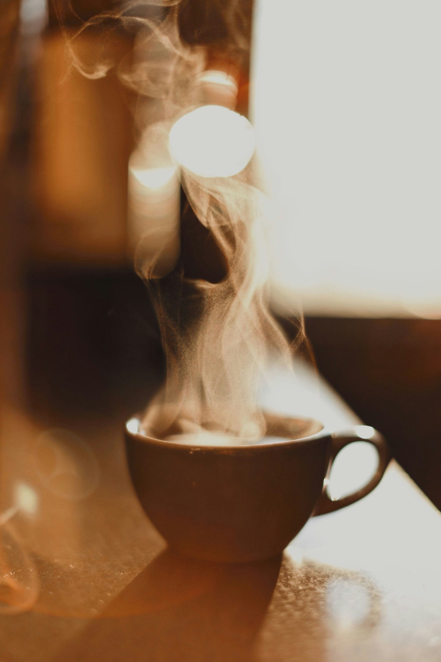 Steaming cup of coffee on a wooden table with a blurred background