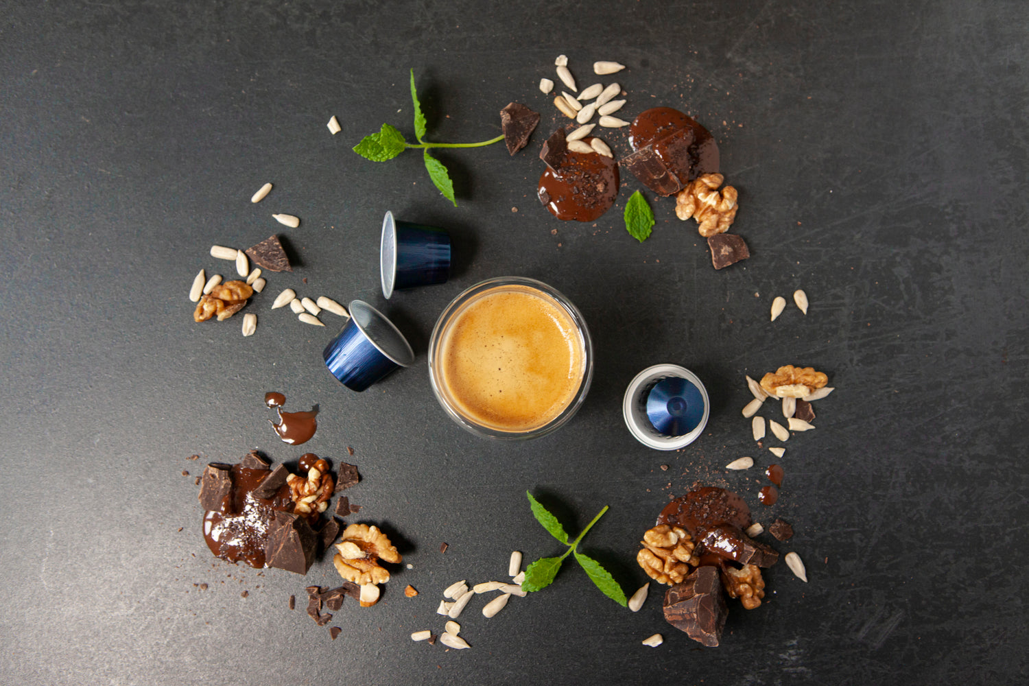 Cup of coffee with coffee capsules and nuts on a dark surface