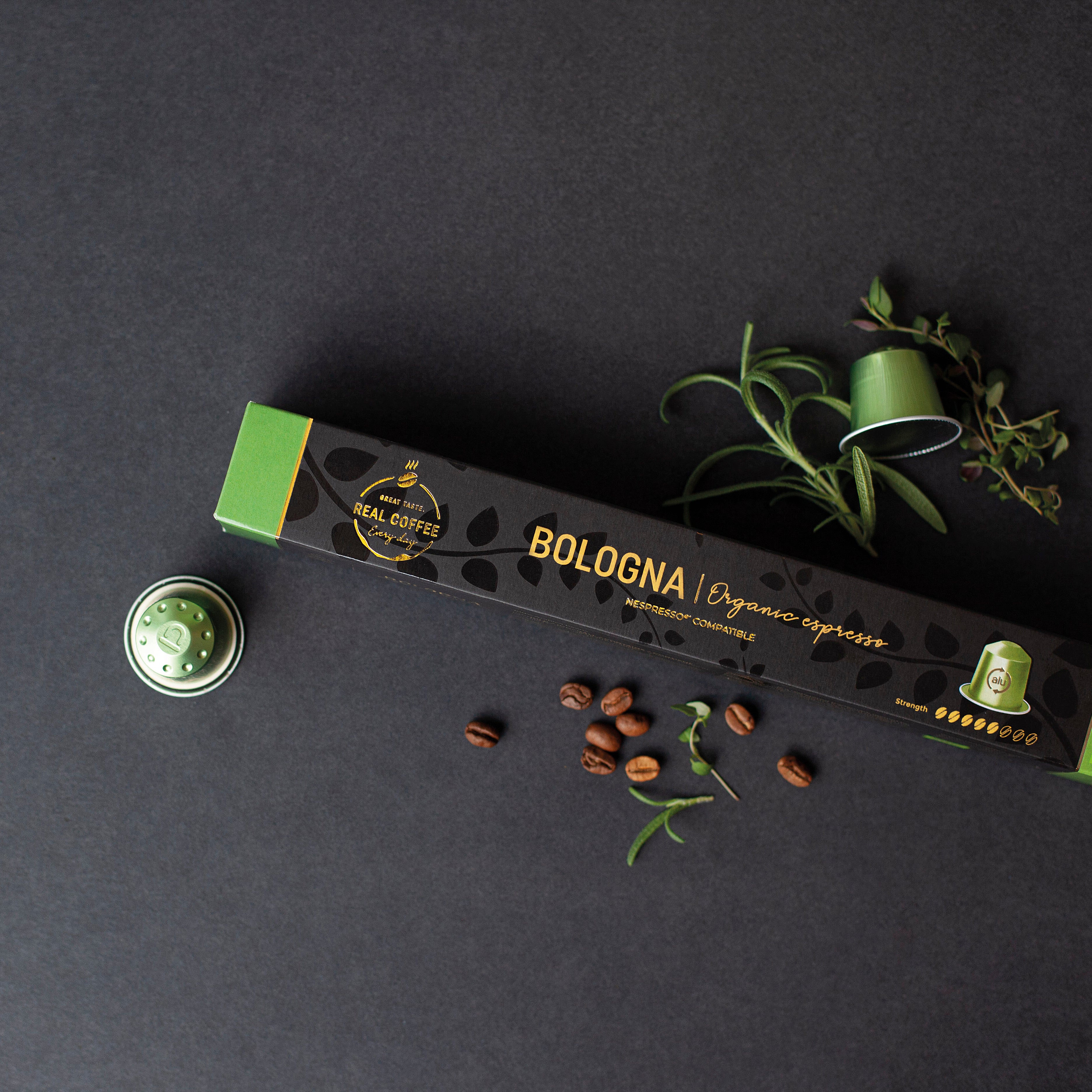 Espresso Bologna Organic Nespresso® Compatible Coffee capsule packaging on a dark surface with coffee beans and a plant.