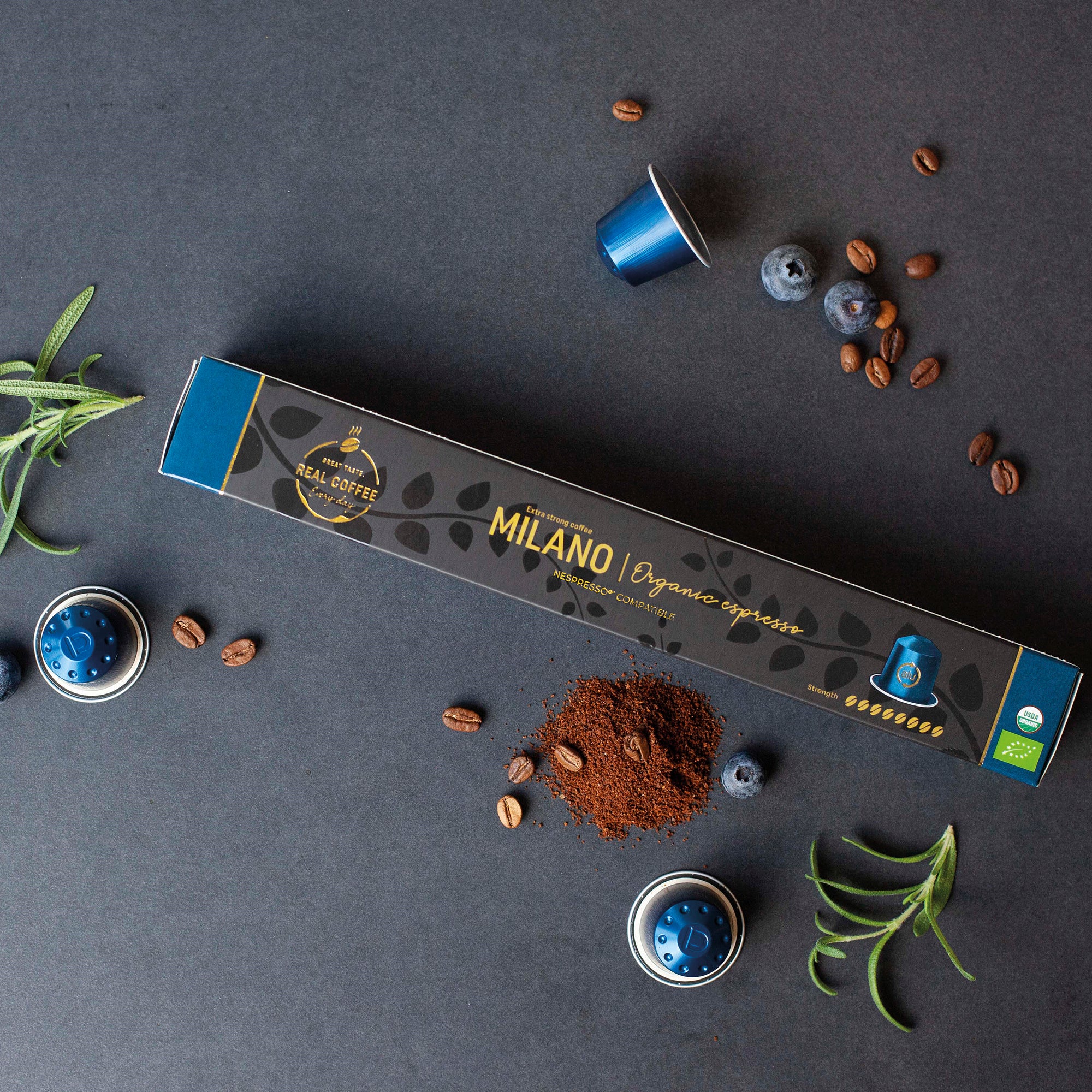 Espresso Milano Organic Nespresso® Compatible Coffee Capsules packaging with coffee beans, blueberries, and capsules on a dark surface